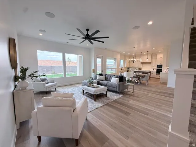 Spacious open-concept living area featuring light wood-finish flooring, a large ceiling fan, and recessed lighting