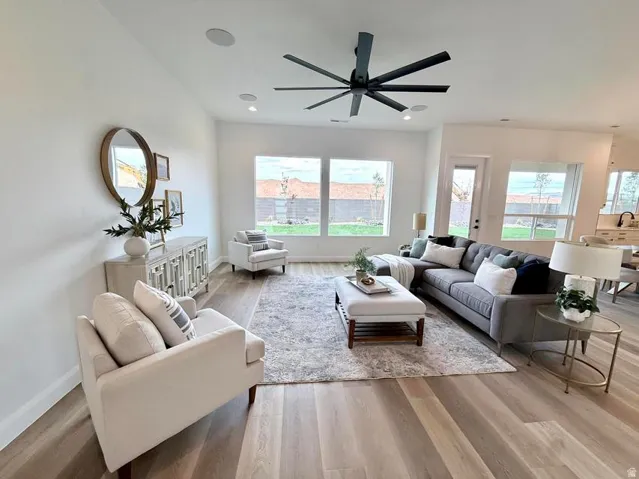 Open-concept living area featuring wood-finish flooring, a large ceiling fan with multiple blades, recessed lighting, and multiple windows