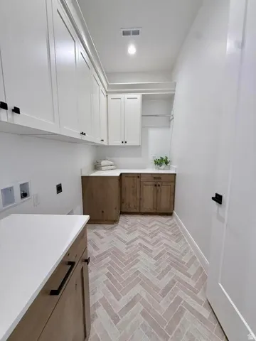 Herringbone tile flooring defines this laundry space, complemented by extensive white cabinetry with matte black hardware