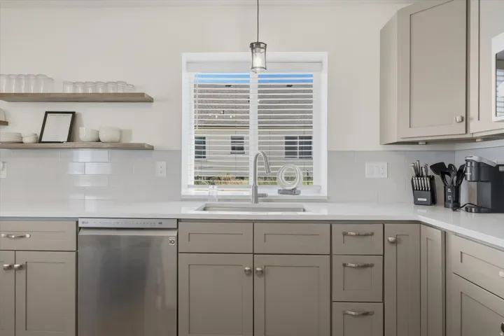 Modern kitchen featuring light gray cabinetry, stainless steel dishwasher, white subway tile backsplash, and light-toned countertops
