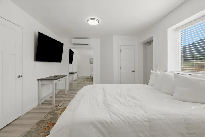 White walls featuring wood-finish flooring, a window with horizontal blinds, and a built-in wall unit