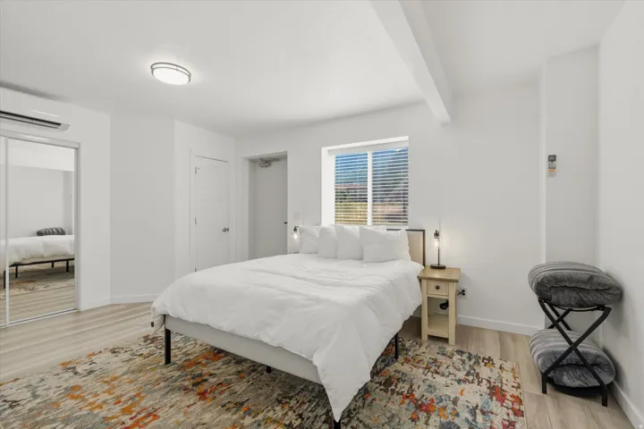 Bright interior space featuring light wood-finish flooring, a window with blinds, and a built-in air conditioning unit