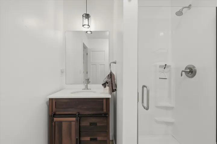 Bathroom featuring a dark wood-finish vanity with a white countertop and undermount sink, brushed nickel faucet, and a glass-enclosed shower with a built-in shelf