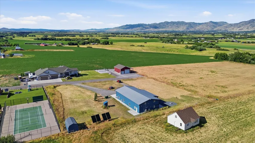 Expansive property featuring a modern ranch-style residence, a large blue industrial-style building, a red barn, a white outbuilding, and a fenced hardcourt