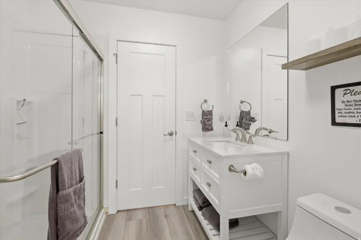 Bright white bathroom featuring a glass-enclosed shower with an integrated shelf, a paneled door, and wood-finish flooring