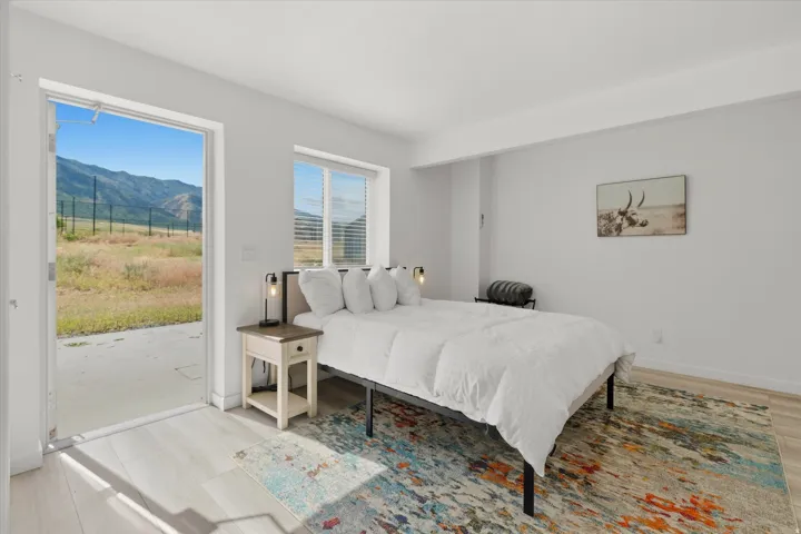 Bedroom featuring a large open doorway to an outdoor patio with mountain scenery, a window with horizontal blinds, and light wood-finish flooring