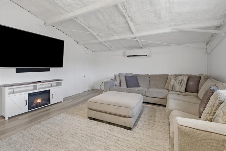 Spacious room featuring a wall-mounted television, a built-in electric fireplace, wood-finish flooring, and white walls