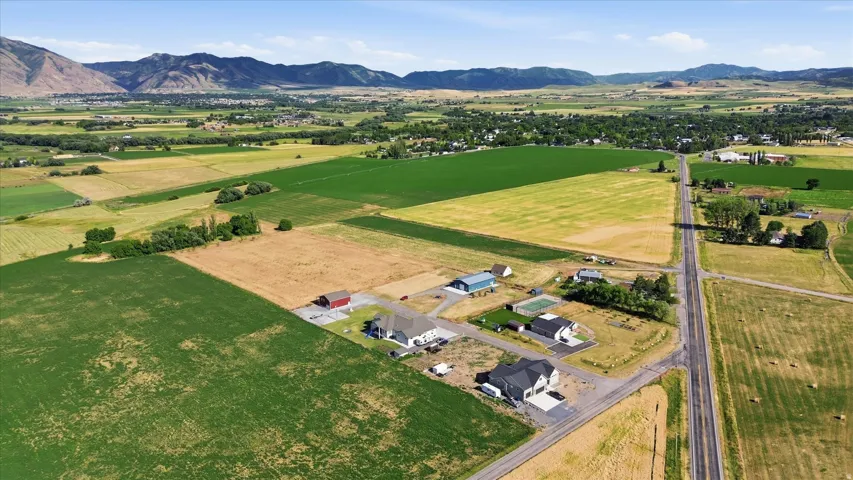 Expansive rural landscape featuring a mix of agricultural fields and scattered residential properties, bordered by distant mountains