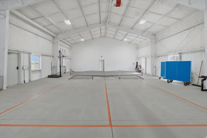 Spacious indoor court featuring concrete flooring with orange court lines, high ceilings with exposed trusses, and bright overhead lighting