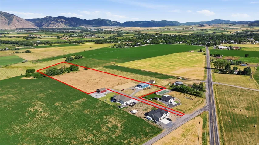 Expansive rural property featuring a large open field, mature trees, and mountainous terrain in the background