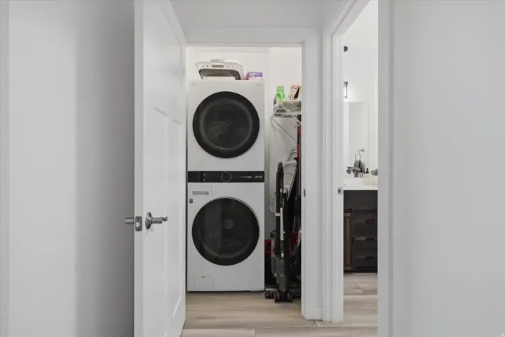 Dedicated laundry area featuring stacked front-loading appliances and light wood-finish flooring