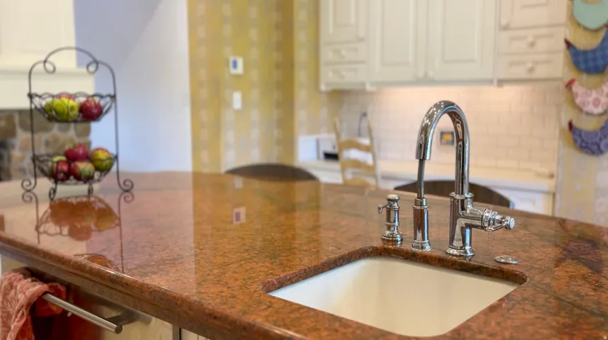 Kitchen island featuring a polished granite countertop, undermount sink, and polished chrome faucet