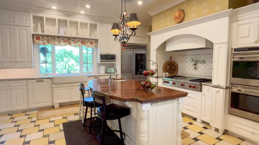 White kitchen featuring a central island with a polished countertop, stainless steel appliances, a farmhouse sink, and a tiled backsplash
