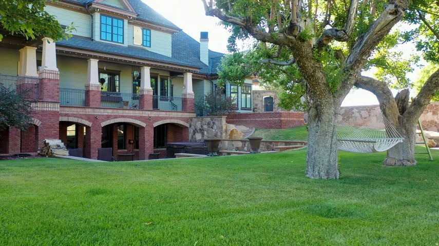 Expansive green lawn with mature trees and a multi-level architectural design featuring brick accents and a stucco finish