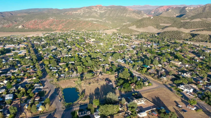 Expansive aerial capturing a town nestled within a broad valley, featuring numerous residential properties and a central pond