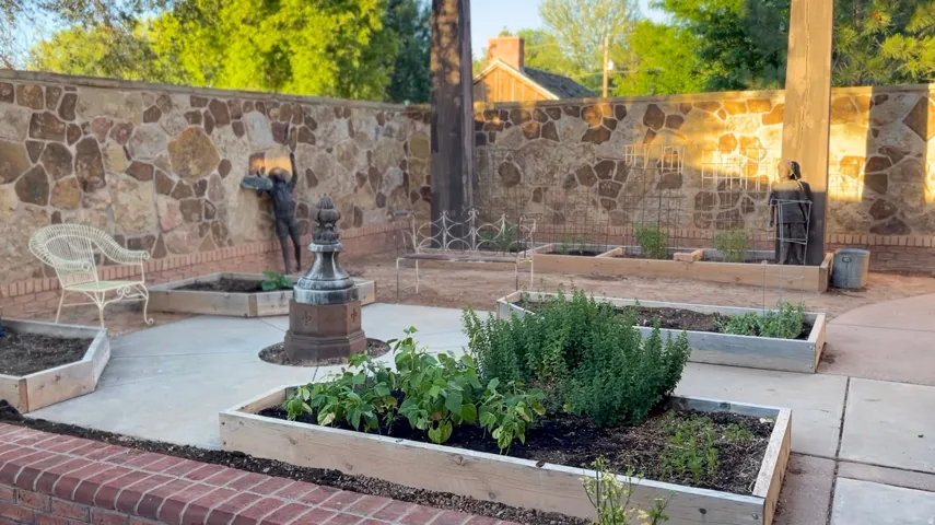 Stone accent wall surrounding a patio space featuring multiple raised garden beds, a central decorative element, and a brick border