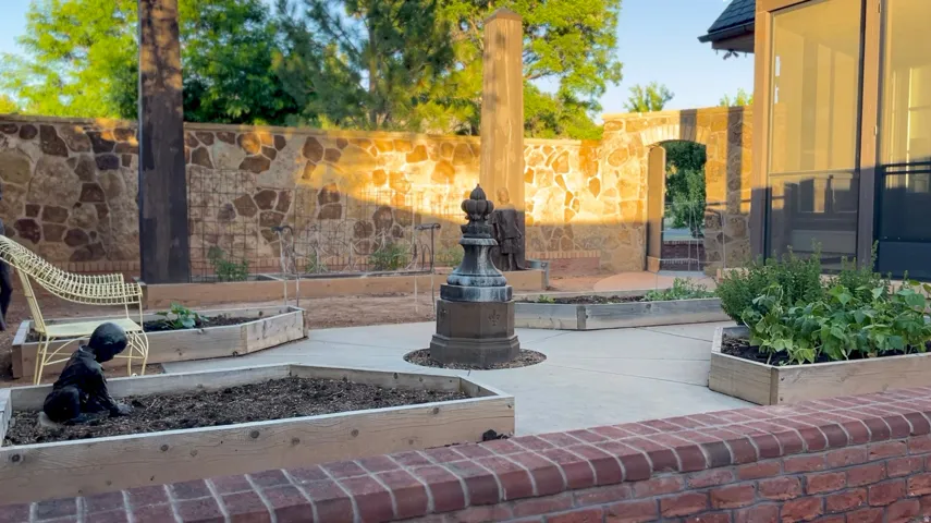 Paved patio area featuring multiple raised wooden garden beds, a stone accent wall, and a brick knee wall