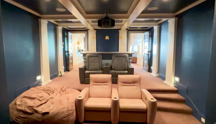 Dedicated media room featuring a coffered ceiling, wall-mounted projector, and built-in bar