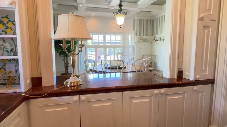 Kitchen pass-through featuring rich red-brown countertops and white cabinetry with panel detailing