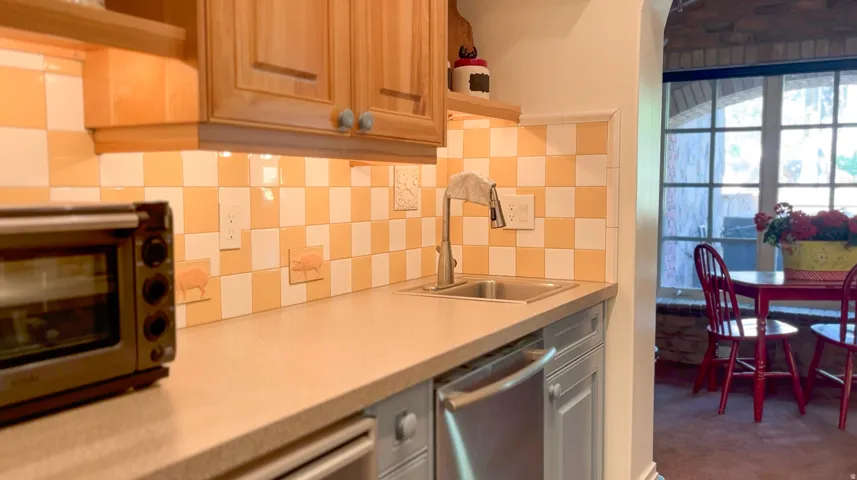 Kitchen featuring light wood cabinetry, stone-look countertops, and a checkered tile backsplash