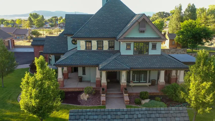 Multi-level residential exterior featuring a prominent teal facade, a dark shingle roof, and a covered front porch with brick pillars