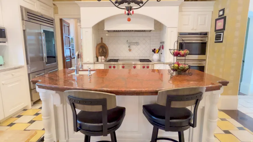 Kitchen featuring a large island with a substantial countertop, white cabinetry, integrated stainless steel appliances, a range oven with a tile backsplash, and decorative patterned flooring