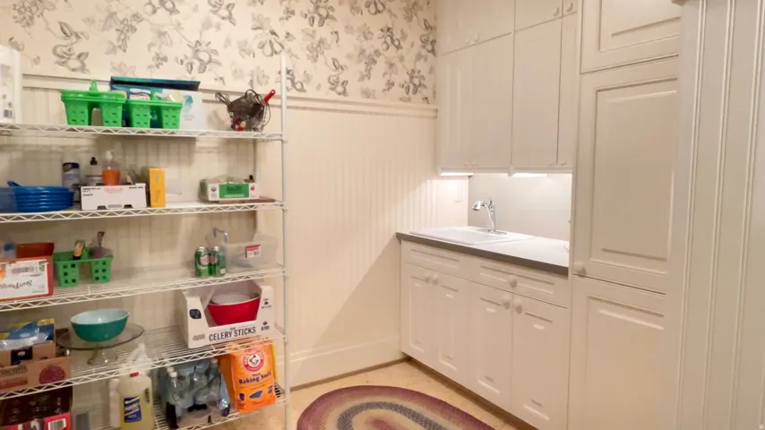 Utility room featuring white cabinetry, integrated sink with chrome faucet, task lighting, and patterned wallpaper