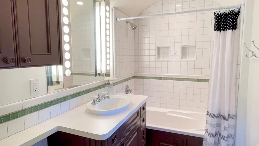 Bathroom featuring a white tile shower surround with green accent trim, an arched ceiling, and integrated shower niches