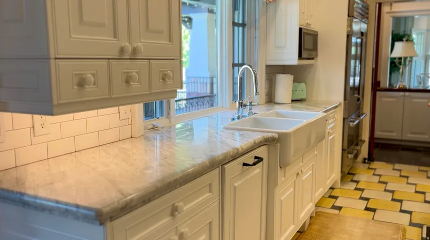 Kitchen featuring white cabinetry, a double basin farmhouse sink, light-toned countertop, subway tile backsplash, and built-in stainless steel appliances