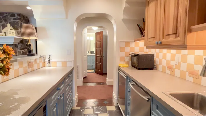 Galley kitchen featuring light blue base cabinetry, natural wood-finish upper cabinetry, and a checkerboard tile backsplash