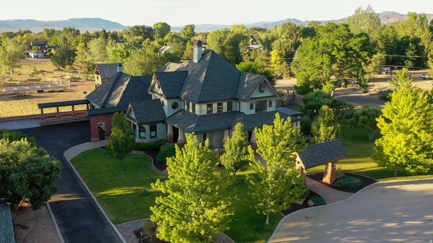 Stately residence featuring a multi-gabled roofline, stone and siding exterior, expansive driveway, and mature landscaping