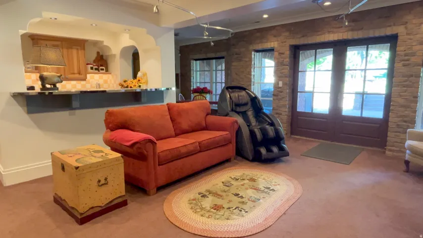 Lower-level entertainment space featuring a wet bar with wood cabinetry and tile backsplash, double glass-paneled doors, stone accent wall, and recessed lighting