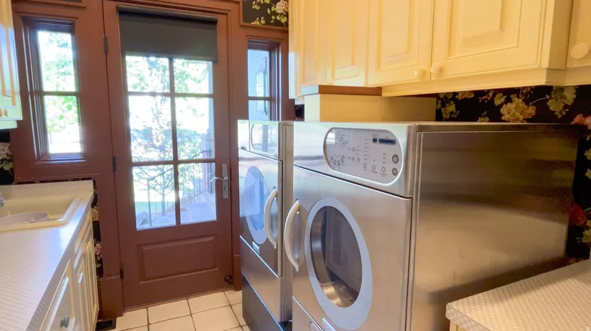 Laundry area featuring a full-light paneled door, two windows, upper cabinetry with white hardware, and a utility sink