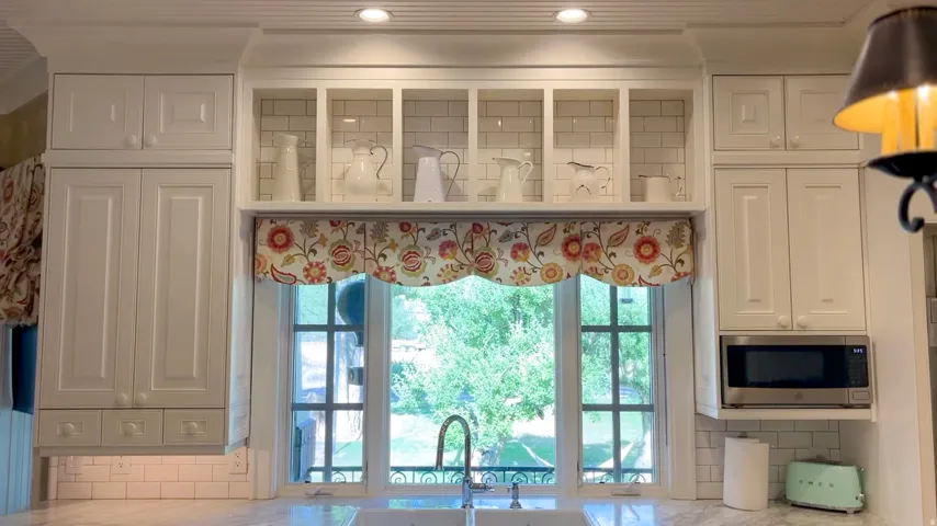 White cabinetry with recessed panel doors, subway tile backsplash, and integrated shelving above a kitchen sink with a gooseneck faucet