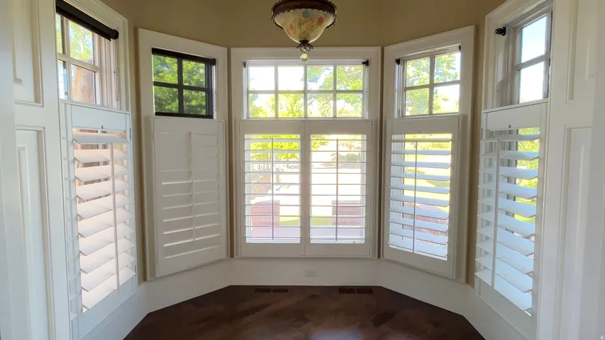 Bay window with white plantation shutters, wood-finish flooring, and an ornate ceiling fixture