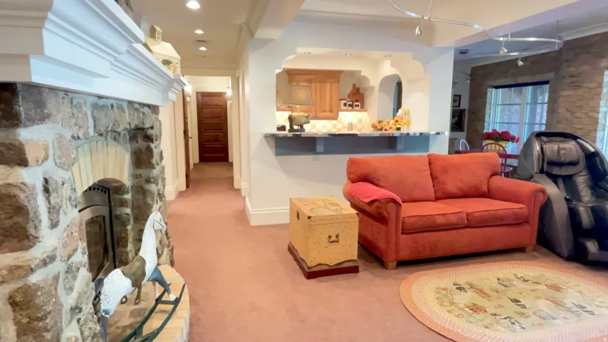 Stone fireplace with a white mantel, recessed lighting, and a kitchen pass-through featuring wood cabinetry and a countertop