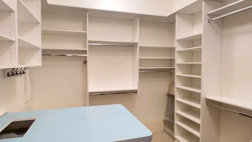 Walk-in closet featuring white built-in shelving, multiple hanging rods, and a central island with a light blue countertop