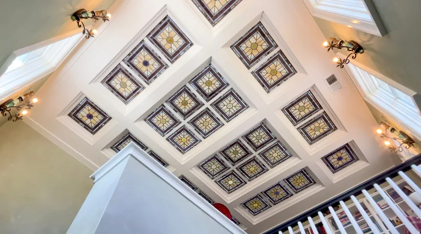 Coffered ceiling featuring multiple decorative panels and recessed lighting, complemented by multiple wall sconces and integrated skylights