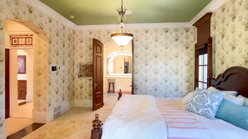 Bedroom featuring patterned wallpaper, a green ceiling, crown molding, and an arched entryway with stained glass