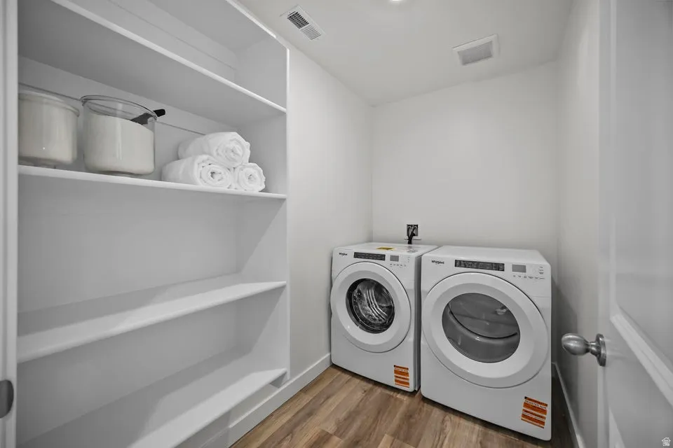 Dedicated laundry space featuring wood-finish flooring, white walls, and built-in shelving