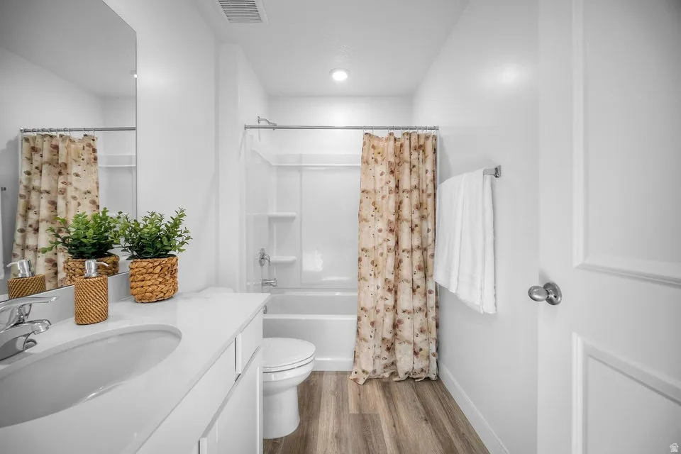 Bathroom featuring a white vanity with an integrated sink, polished chrome faucet, rectangular wall mirror, and wood-finish flooring