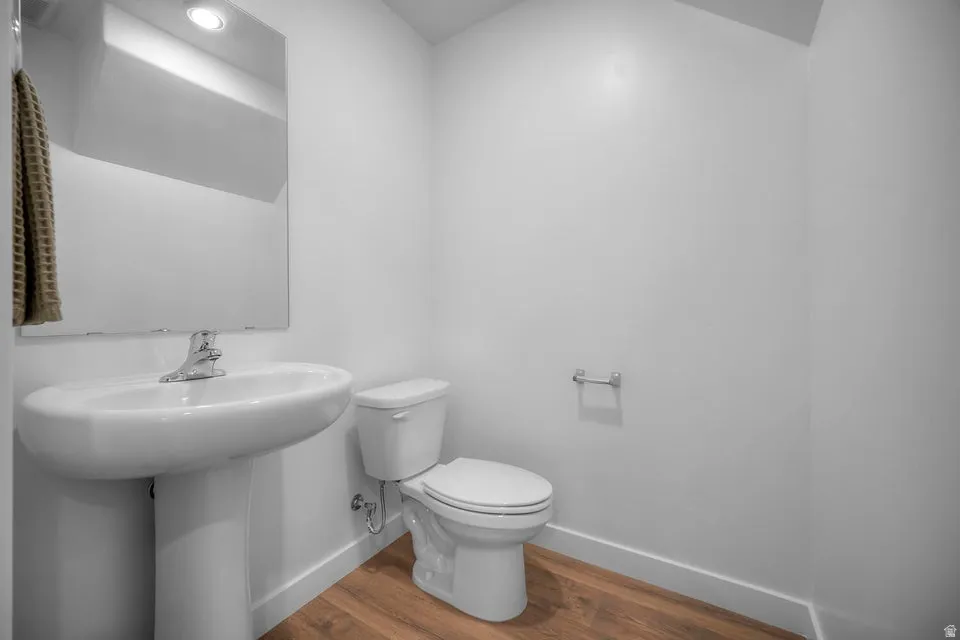 Bathroom featuring a pedestal sink, a toilet, wood-finish flooring, and a wall-mounted mirror
