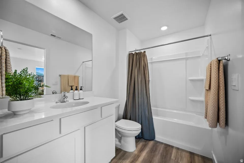 Bathroom featuring a white vanity with an integrated sink, a full-width mirror, and wood-finish flooring
