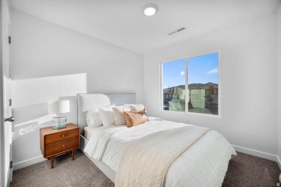 Bedroom featuring a large window, white walls, and neutral carpet flooring