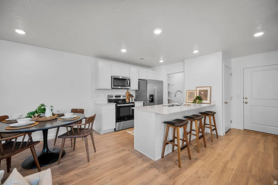 Open-concept kitchen and dining area featuring light wood-finish flooring, white cabinetry, stainless steel appliances, a white countertop island with seating, and recessed lighting