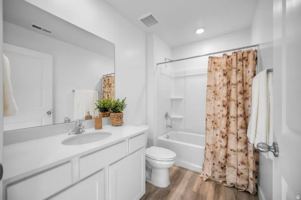 Contemporary bathroom featuring a single vanity with an integrated sink, white cabinetry, a large frameless mirror, a white bathtub with a shower kit, and wood-finish flooring