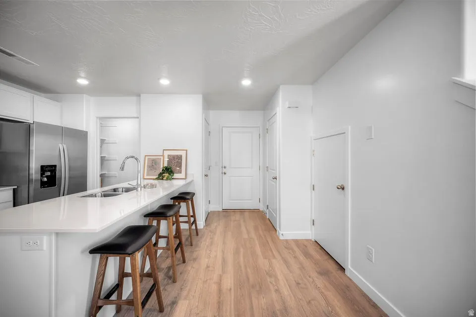 Open-concept kitchen featuring a spacious peninsula with seating, stainless steel appliances, a built-in pantry, and wood-finish flooring