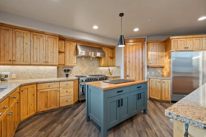 Spacious kitchen featuring natural wood cabinetry, granite countertops, stainless steel appliances, and a central island with a wood-finish top