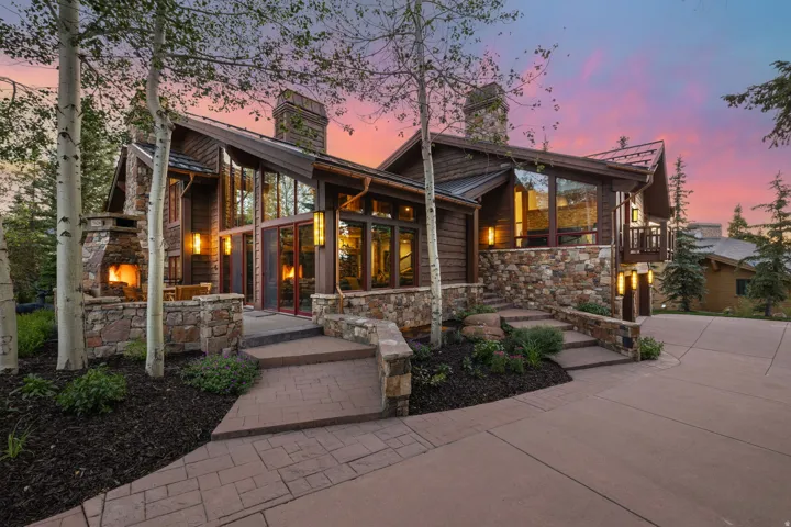 Stone and wood-sided exterior featuring multiple large windows, an outdoor fireplace, a stone retaining wall, and a stamped concrete driveway