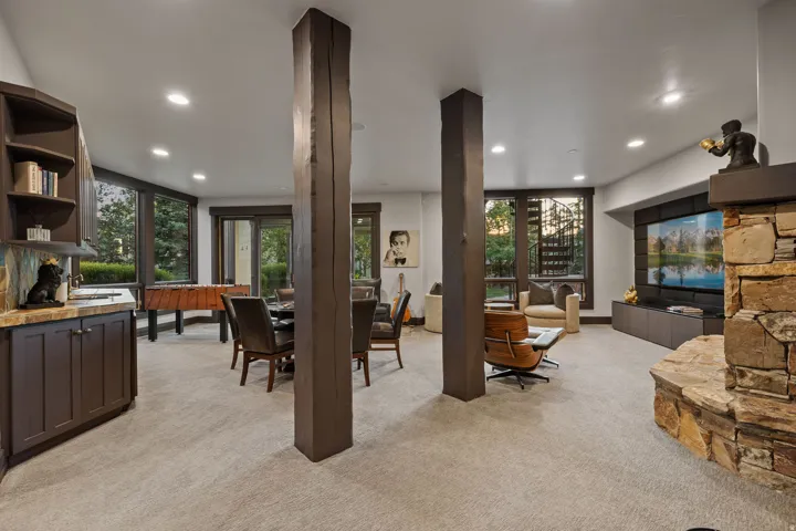 Lower level entertainment space featuring a natural stone fireplace, a wet bar with dark wood cabinetry and a stone countertop, and recessed lighting